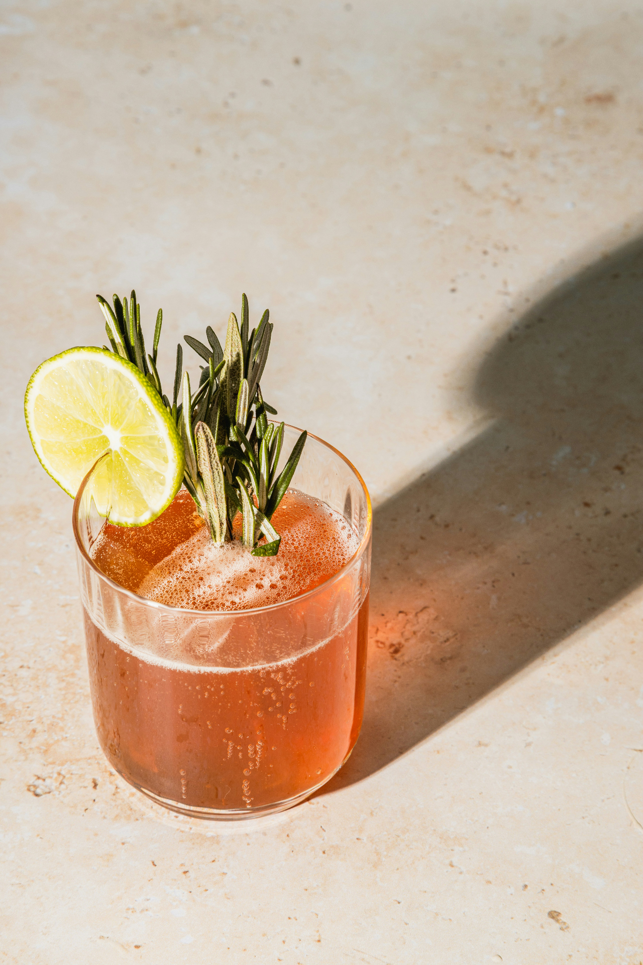 Een cocktail met limoen en rozemarijn op een zonnig stenen oppervlak
